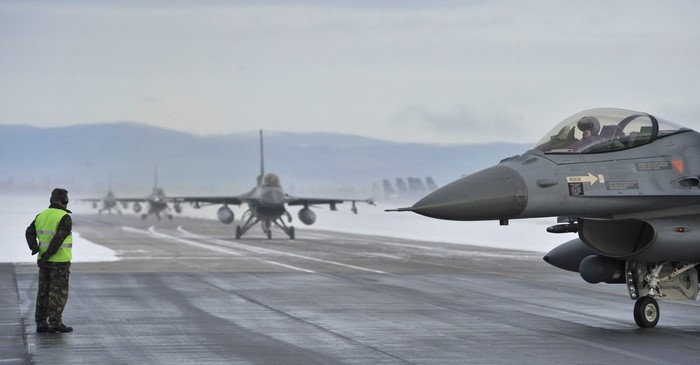 F-16 Fighting Falcon jets on a snowy runway with a ground crew member