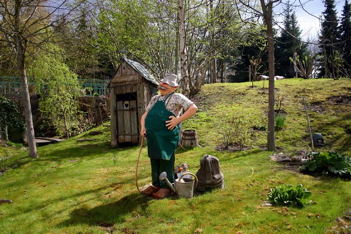 Garden gnome with watering can near outhouse