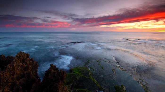 Ocean sunset with colorful clouds and rocky shore