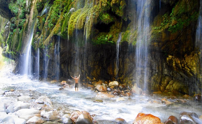 Man standing under waterfalls in a rocky gorge