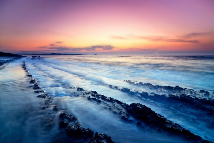 Ocean waves crashing on rocky shore at sunset