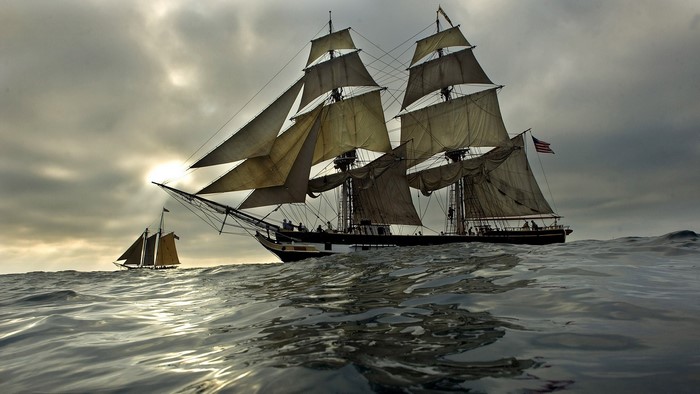 Two sailing ships on the ocean under a cloudy sky
