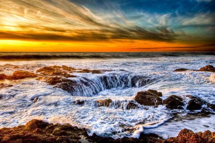 Ocean waves crashing on rocky shore at sunset