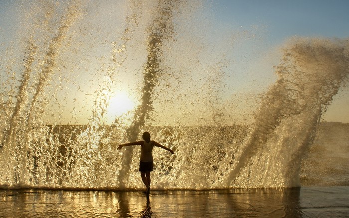 Person standing in ocean waves at sunset