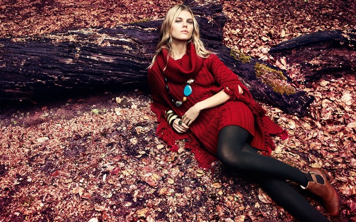 Woman in red dress lying on fallen leaves near a log