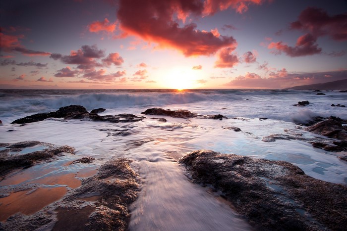 Sunset over the ocean with waves crashing on rocks