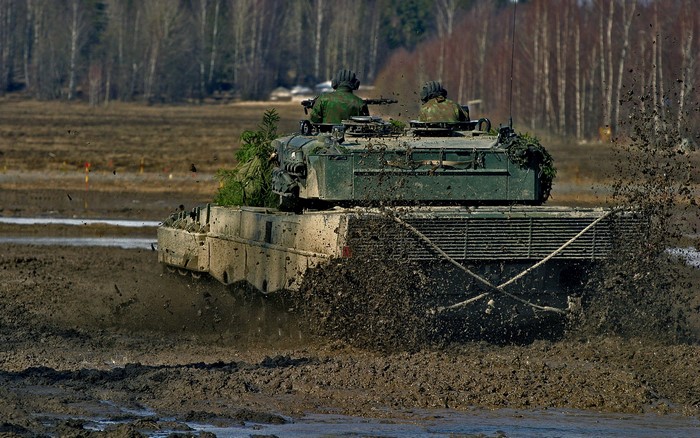 Tank driving through mud with soldiers