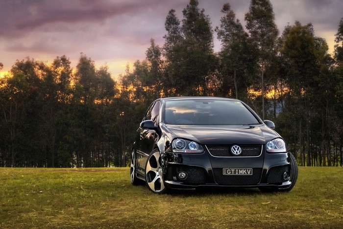 Black Volkswagen Golf GTI parked on grass at sunset