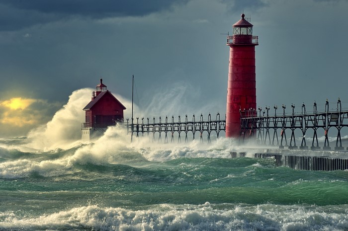 Two red lighthouses on a pier during a storm with large waves