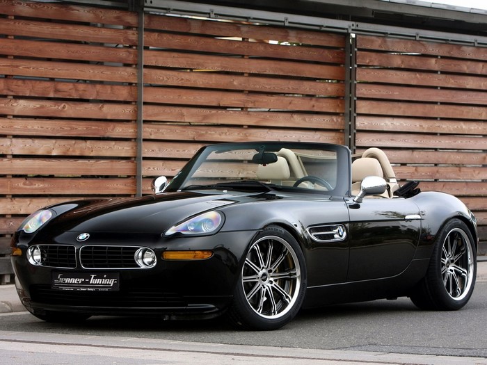 Black BMW Z8 convertible parked in front of a wooden wall