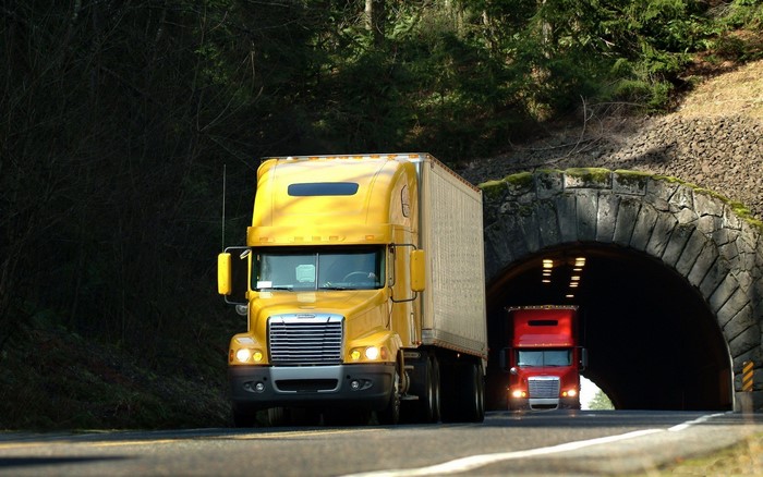 Yellow and red Freightliner trucks on a road near a tunnel