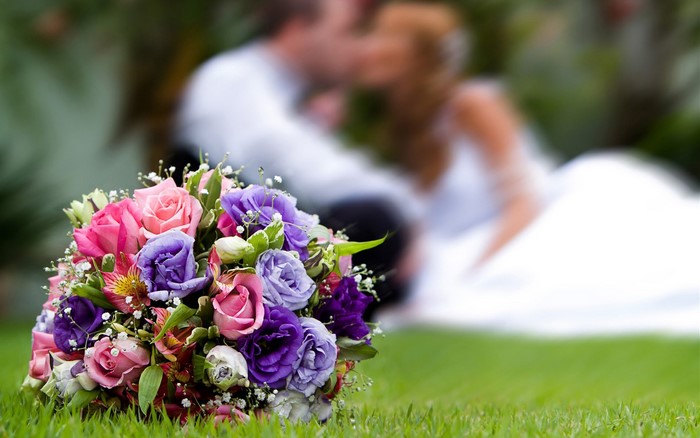 Wedding bouquet with couple kissing in background
