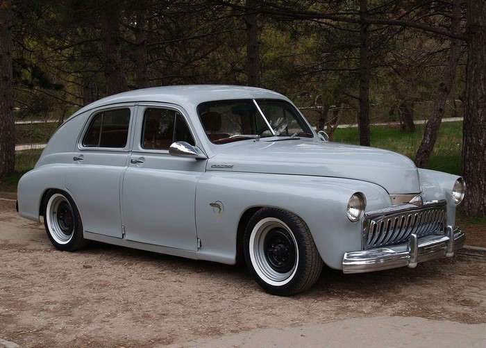 Retro grey sedan parked on dirt road near trees