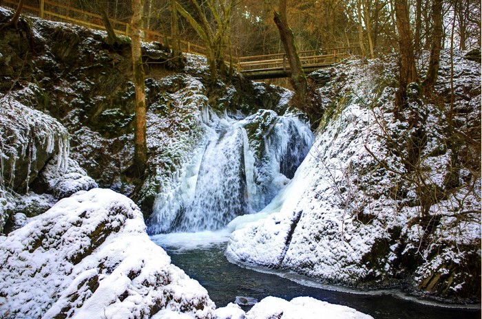 Frozen waterfall in a snowy forest with a wooden bridge