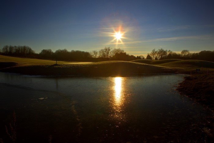 Sun reflecting on frozen pond with golf course background