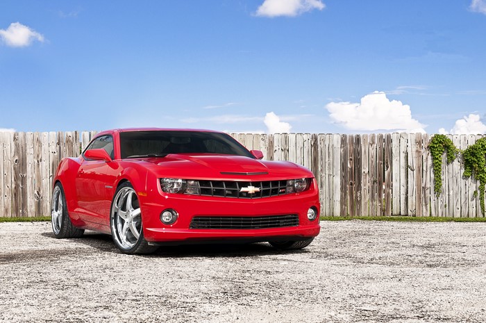 Red Chevrolet Camaro parked near a wooden fence
