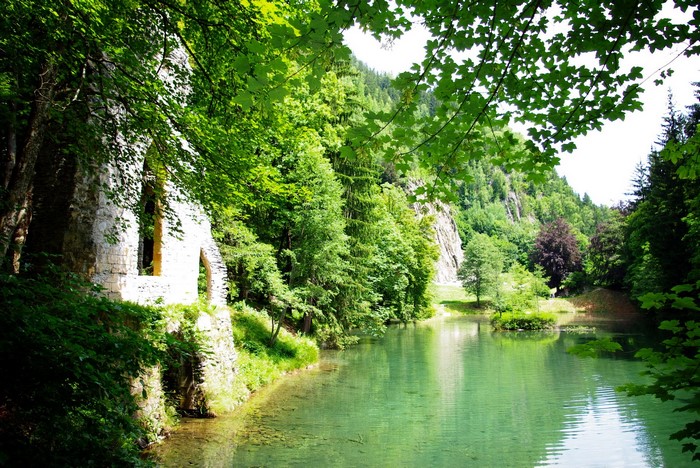 Ruins by a clear lake in a lush green forest