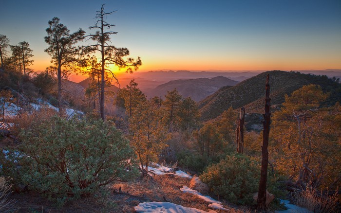 Sunset over mountainous landscape with trees and snow