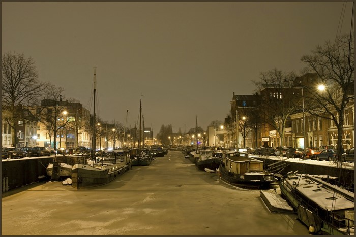 Frozen canal with boats in a Dutch city at night