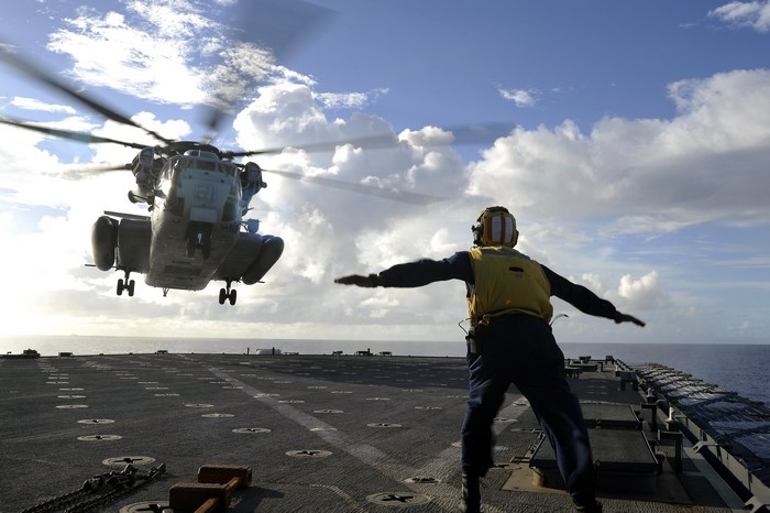 Helicopter landing on aircraft carrier with deck crew