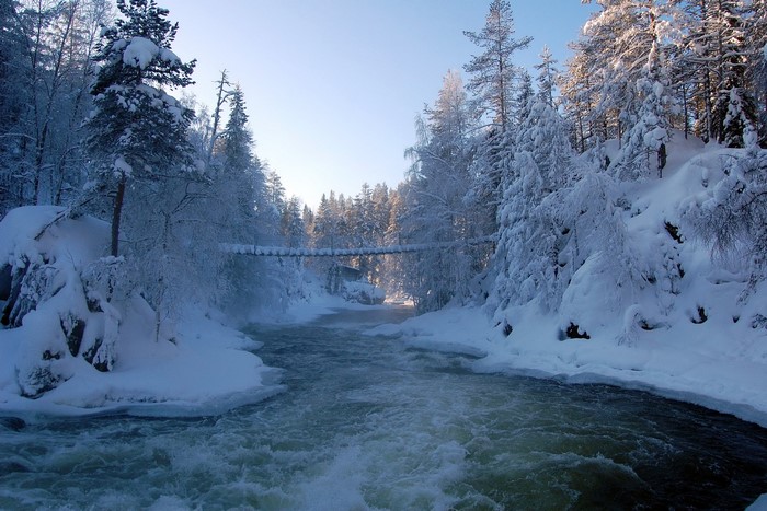 Winter river flowing through a snow-covered forest with a suspension bridge