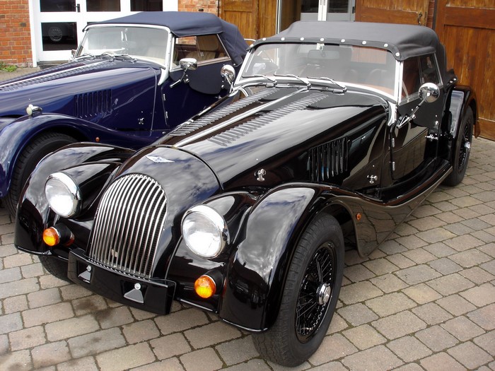 Two Morgan cars, one black and one blue, parked outside