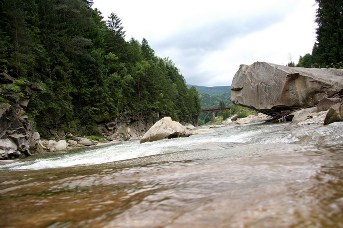River flowing through a rocky, forested mountain landscape with a bridge in the distance
