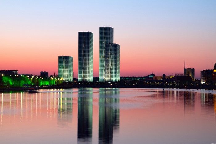 Four illuminated skyscrapers reflected in a calm river at dusk