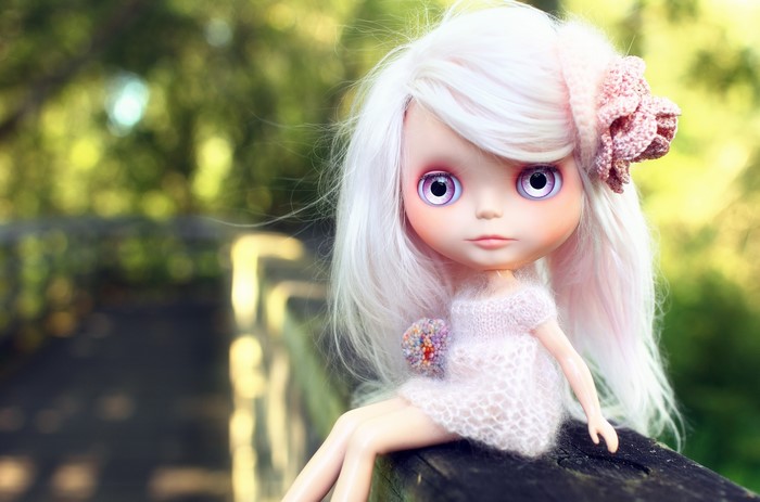 Doll with white hair and pink dress sitting on a wooden railing