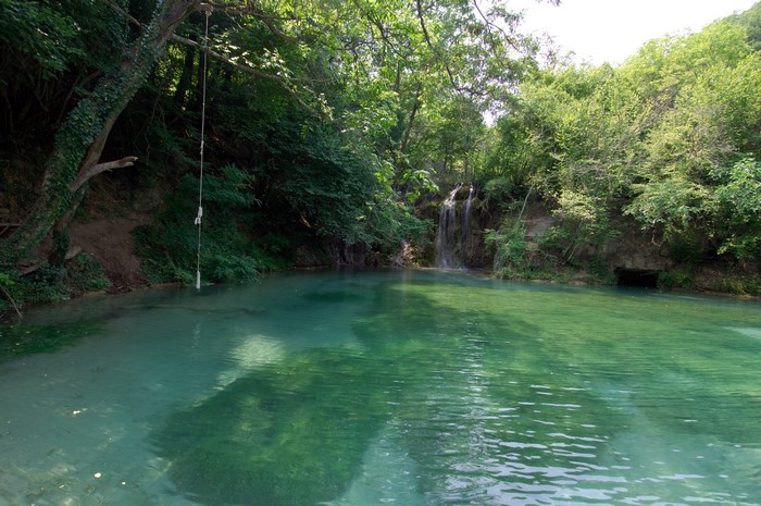 Rope swing over a clear turquoise pool with a waterfall