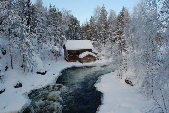 Wooden cabin by a river in a snowy forest
