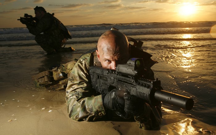 Soldiers aiming rifles on a beach at sunset