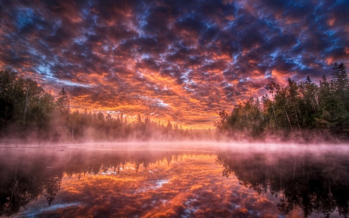 Sunrise over a misty lake with forest reflection