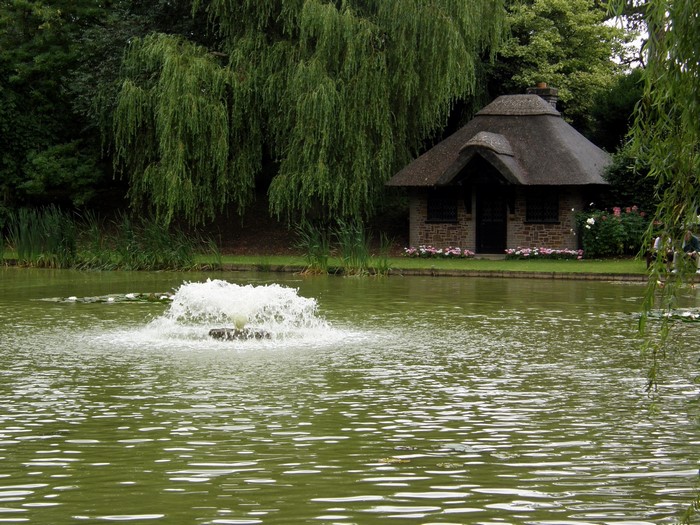 A fountain in a pond near a thatched-roof cottage