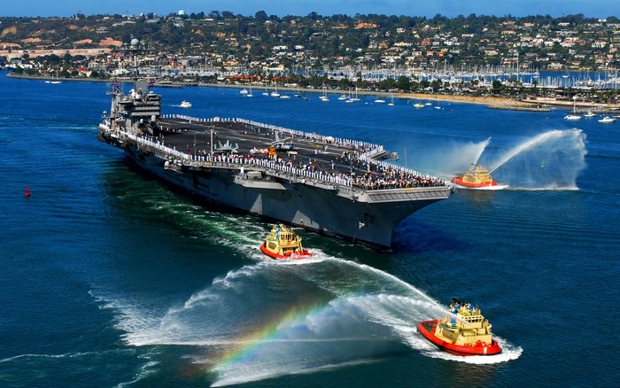 Aircraft carrier entering harbor with tugboats spraying water