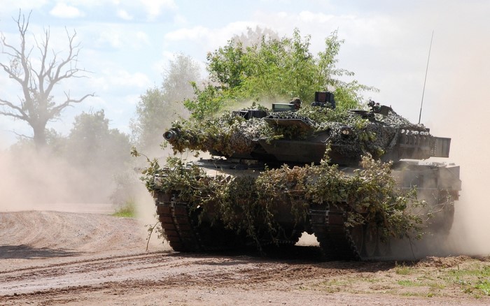 Camouflaged tank driving on a dirt road