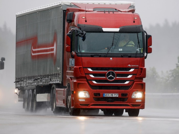 Red Mercedes-Benz Actros truck driving on a wet road
