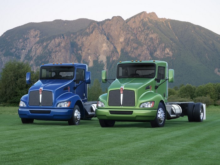 Two Kenworth trucks on a grassy field with mountains