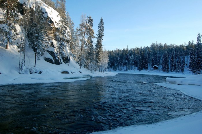 Winter river flowing through a snowy forest with a small cabin