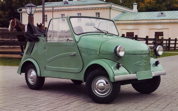 Green convertible car with horses and building