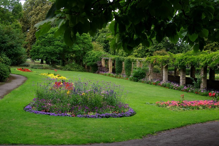 A beautiful park with flower beds and a stone pergola