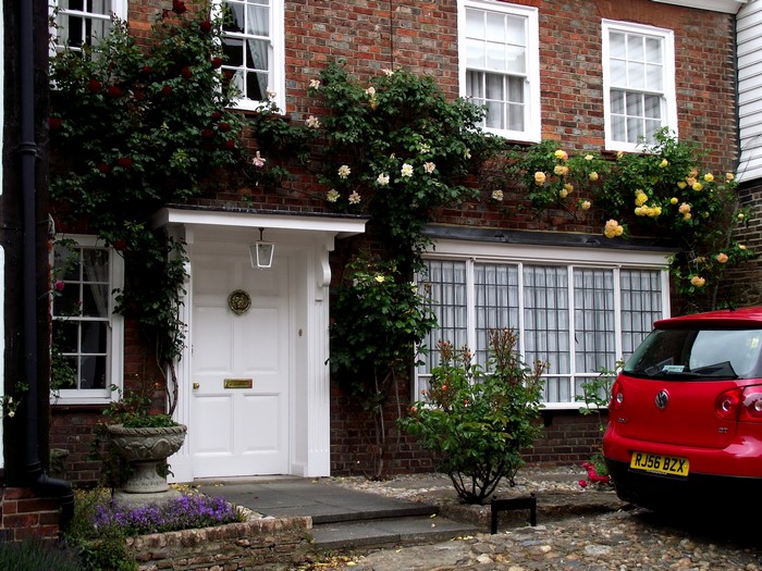 Red Volkswagen Golf parked outside a brick house with roses in the UK