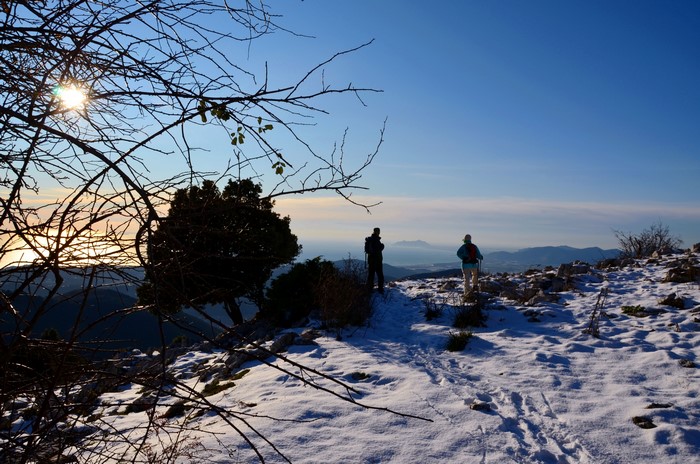 Two hikers on a snowy mountain overlooking the sea