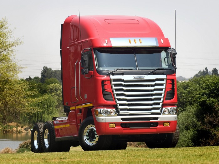 Red Freightliner Cascadia semi-truck parked on grass