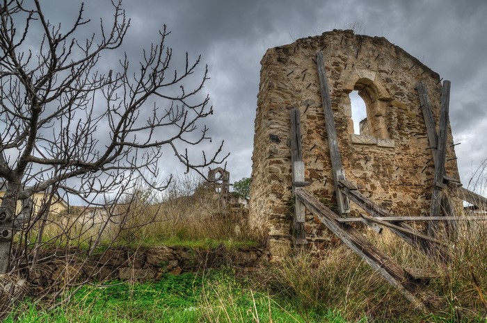 Stone ruins with a bare tree under a cloudy sky