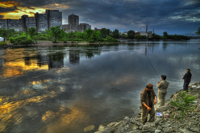 People fishing on a river with city skyline