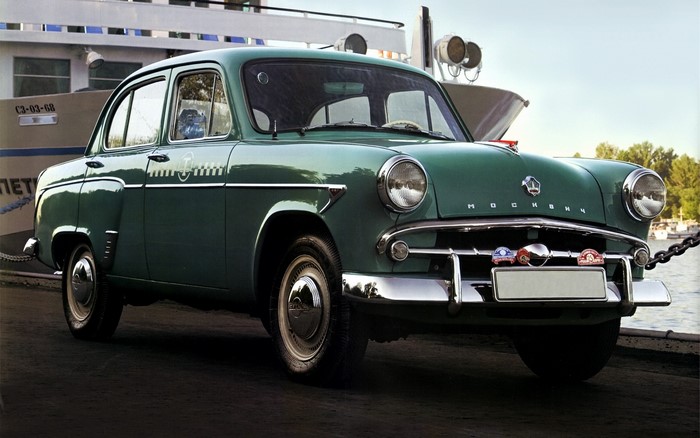 Green Moskvich car parked by a boat