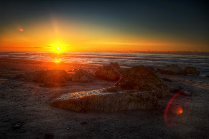 Sunset over the ocean with rocks on the beach