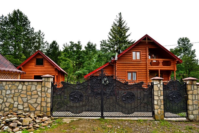 Log houses behind a stone wall and ornate gate in Zakarpattia, Ukraine
