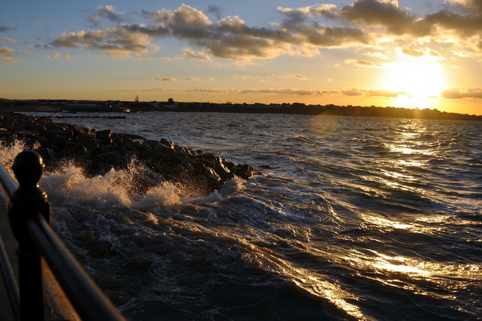 Sunset over the ocean with waves crashing on rocks